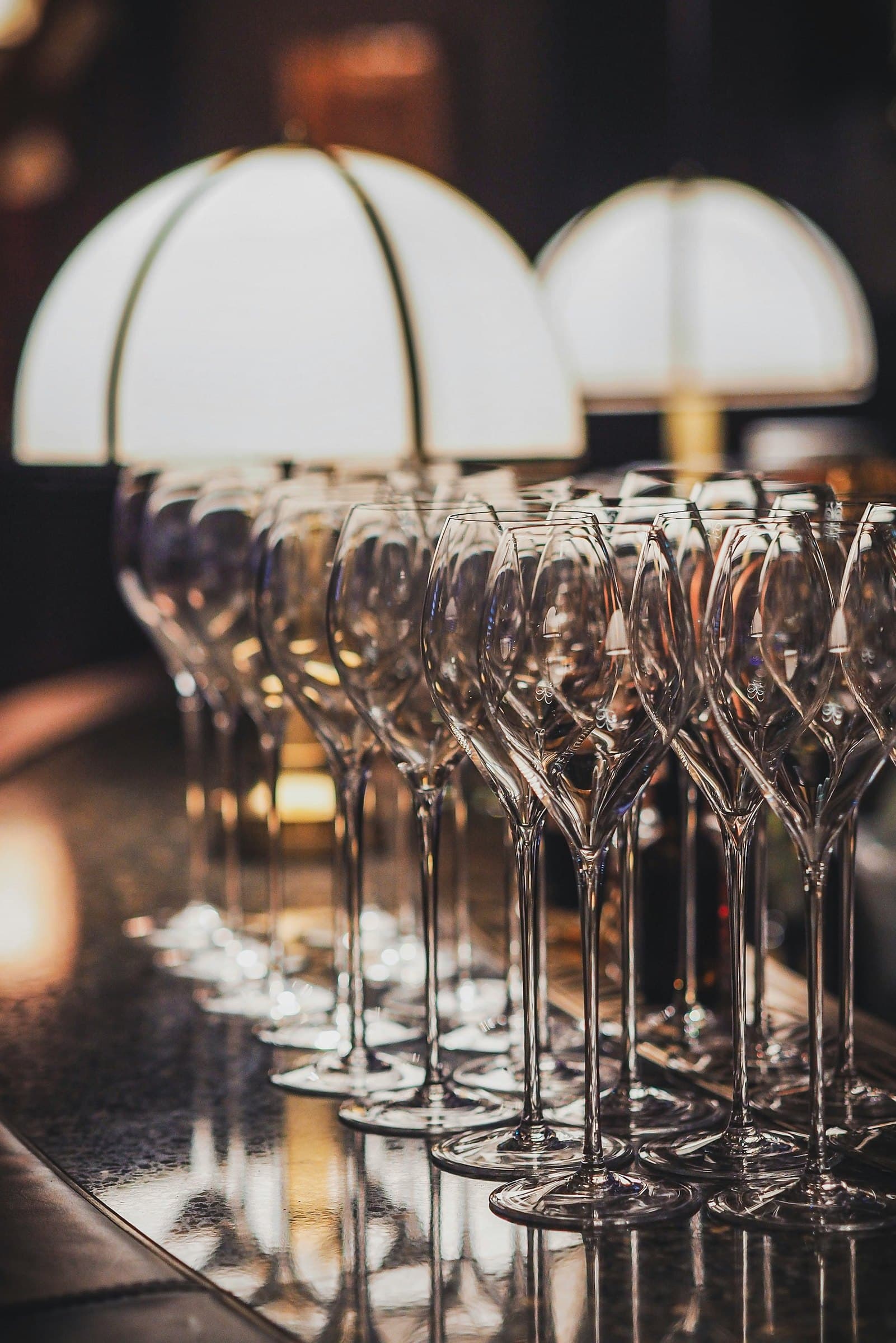 Rows of empty stemmed glassware arranged beneath warm pendant lights