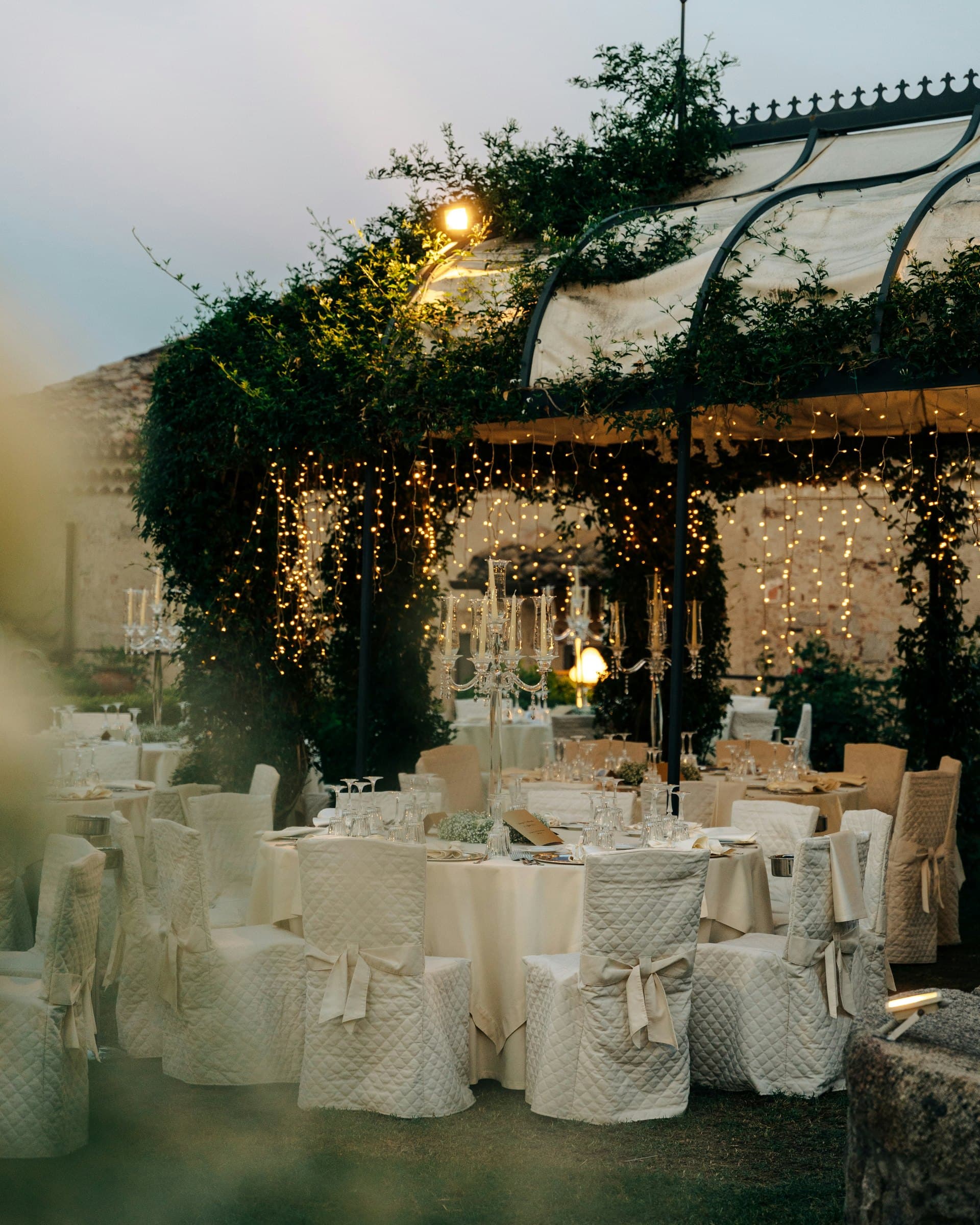 Outdoor reception with round tables, white chairs, and overhead greenery